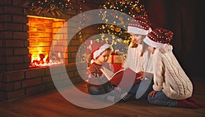 Family mother and children read a book at christmas near firep