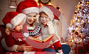 Family mother and children read a book at christmas near firep