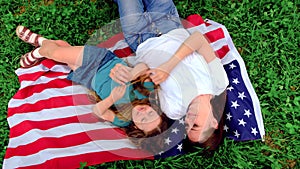 family Mother and daughter lying on national USA flag outdoors over summer green grass - american flag, country