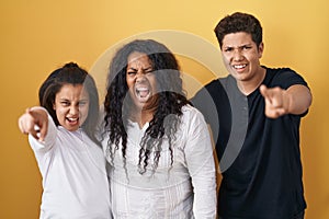 Family of mother, daughter and son standing over yellow background pointing displeased and frustrated to the camera, angry and