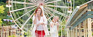 Family. Mother and daughter spend boring time together in an amusement Park. Ferris wheel in the background. Panorama. Concept of