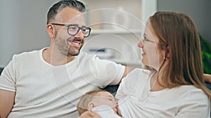 Family of mother, father and baby breastfeeding sitting on the sofa at home