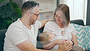 Family of mother, father and baby breastfeeding sitting on the sofa at home