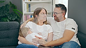 Family of mother, father and baby breastfeeding sitting on the sofa at home