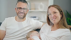 Family of mother, father and baby breastfeeding sitting on the sofa at home