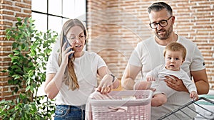 Family of mother, father and baby doing laundry speaking on the phone at laundry room