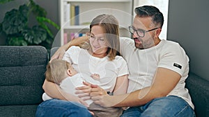 Family of mother, father and baby smiling sitting on the sofa at home
