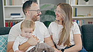 Family of mother, father and baby smiling sitting on the sofa at home