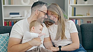 Family of mother, father and baby smiling sitting on the sofa at home