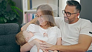 Family of mother, father and baby smiling sitting on the sofa at home