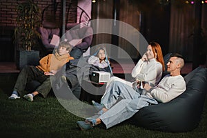 family mother, father and children watch a projector, movies with popcorn in the evening in the courtyard