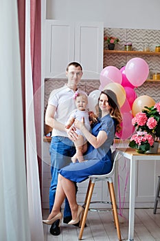 Family mother, father, daughter in the kitchen with a birthday cake and balloons in pink