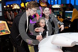 Family mother, father, daughter play arcade games on the computer machines at an amusement park.