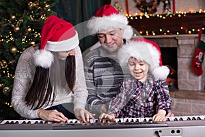 Family - mother, father and kid wearing santa hats playing the piano over christmas background