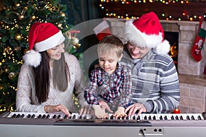Family - mother, father and kid wearing santa hats playing the piano over christmas background