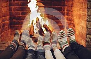 Family mother, father and kids wearing warm woolen socks warming feet by fireplace on Christmas time