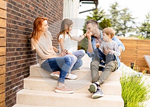 Family with a mother, father, son and daughter sitting outside on the steps of a front porch of a brick house