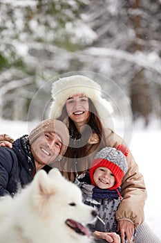 Family of mother, father and son having fun in snowy winter wood with cheerfull pet dog.