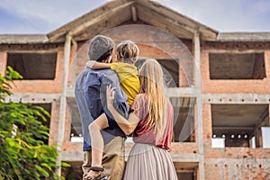 Family mother, father and son looking at their new house under construction, planning future and dreaming. Young family