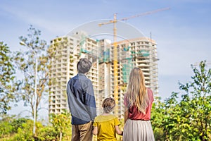 Family mother, father and son looking at their new house under construction, planning future and dreaming. Young family