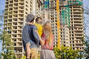 Family mother, father and son looking at their new house under construction, planning future and dreaming. Young family