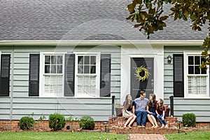 A family with a mother, father, and two daughters sitting outside on the brick steps of a front porch of a small blue