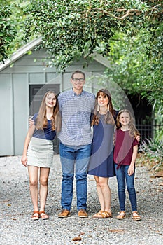 A family of a mother and father and two daughters standing outside in front of a small storage building