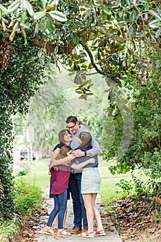 A family of a mother and father and two daughters standing on the sidewalk outside in the summer or fall