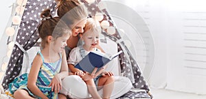 Family mother reading to children book in tent at home