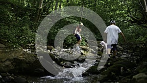 Family of mother and two boys jumping rocks across creek. Creative. Young travelers hiking together in North Carolina