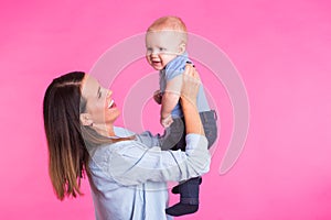 Family, motherhood, parenting, people and child care concept - happy mother holds adorable baby over pink background