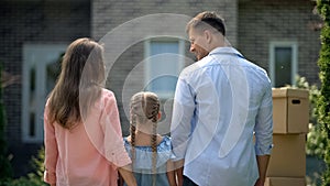 Family moving in, looking at each other in front of new house, back view