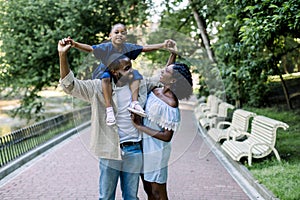 Family in nature in park. Handsome African American man father carrying his little daughter on shoulders, looking at his