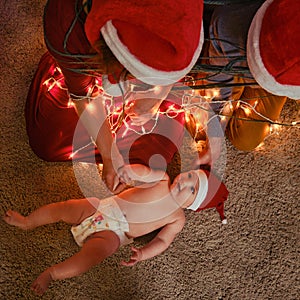 A family with a newborn baby at the Christmas tree in the evening living room. Unfree parents with a small child on New Year Eve