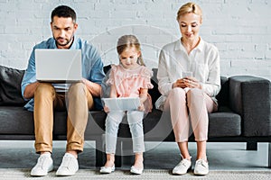 family with one child sitting on couch and using digital