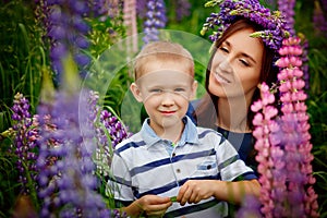Family outdoor recreation on weekends. A happy mother and a cute baby son are hugging tightly among wild flowers in a field.