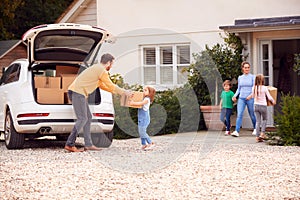 Family Outside New Home On Moving Day Loading Or Unloading Boxes From Car