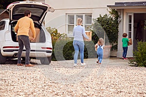 Family Outside New Home On Moving Day Loading Or Unloading Boxes From Car