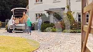 Family Outside New Home On Moving Day Unloading Boxes From Car As Son With Skateboard Runs To Help