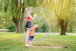 Family parental activity. Young Caucasian mother with child toddler boy doing workout yoga fitness outdoor in park on summer day.