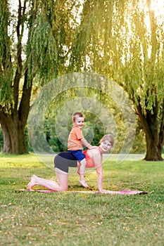Family parental activity. Young Caucasian mother with child toddler boy doing workout yoga fitness outdoor in park on summer day.