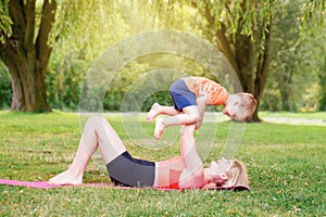 Family parental activity. Young Caucasian mother with child toddler boy doing workout yoga fitness outdoor in park on summer day.