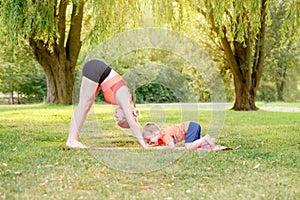 Family parental activity. Young Caucasian mother with child toddler boy doing workout yoga fitness outdoor in park on summer day.