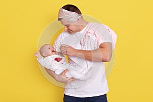 Family, parenthood and people. Father feeding little daughter with baby formula from bottle while standing isolated over yellow