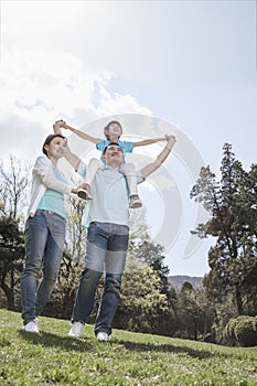 Family in park with son on father's shoulders.