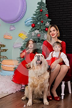 Family photo portrait. Mom and her two children and a white dog in red clothes celebrate the Chistmas, new year. Happy