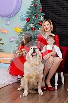 Family photo portrait. Mom and her two children and a white dog in red clothes celebrate the Chistmas, new year. Happy