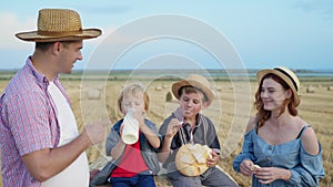 Family at picnic, father with wife and sons eat bread and wash down milk in wheat field