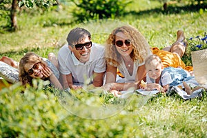 Family picnic on grass in the gardens under gentle shade of trees