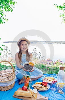 Family picnic in nature. Child girl holding a bowl full of fruits and berries in her hands